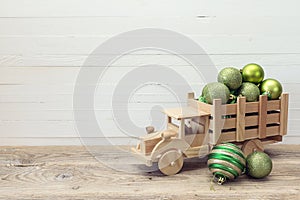 Wooden toy truck with a green Christmas balls in the back on white wooden background. Place for text