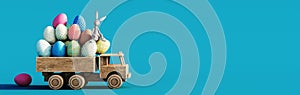 Wooden toy truck loaded with colorful Easter eggs on blue background with copy space.
