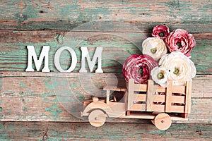 Wooden toy truck with peonies flowers in the back and word MOM on wooden turquoise boards. Space for text