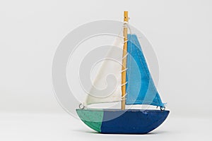 A wooden toy yacht. The toy boat shows signs of use, but the sails are in tact and still attached to the wooden mast. It is paint