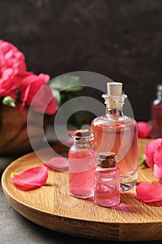 Wooden tray with bottles of rose essential oil and petals on table