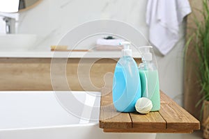 Wooden tray with bottles of shower gels and bath bomb on tub indoors, space for text