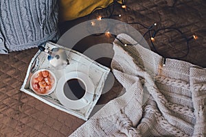 Wooden tray with coffee and kumquat on bed in cozy room.