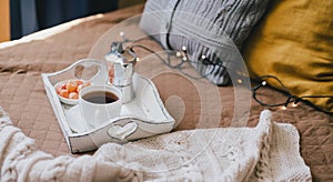 Wooden tray with coffee and kumquat on bed in cozy room.