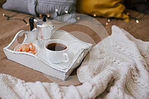 Wooden tray with coffee and kumquat on bed in cozy room.