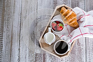 Wooden tray with cup of coffee, freshly baked croissants and fresh strawberry. Copy space, top view
