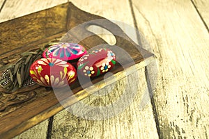 A wooden tray lying on boards with painted eggs.