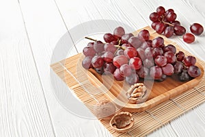 Wooden tray with ripe grapes and nuts on white wooden table