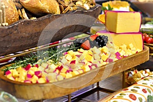 Wooden tray with sliced gouda cheese decorated with strawberries, black grapes and rosemary on the table
