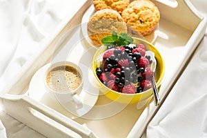 Wooden tray with tasty breakfast on bed. Espresso, banana muffins, cottage cheese with blueberry and raspberry