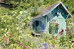 Wooden turquoise summerhouse in beautiful summer garden with lots of blooming flowers