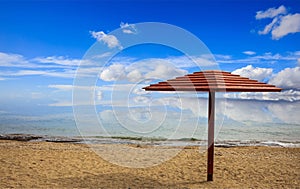 Wooden umbrella on an empty sandy beach. Blue sky and calm sea background.