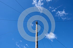 Wooden utility pole and wires against bright blue sky with white clouds.