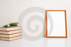 Wooden vertical picture frame mock-up. Books, pine twig, christmas ball and blank portrait frame template on white table indoors
