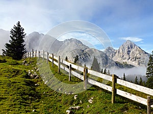 Wooden village fence in perspective on a mountain slope. Rocky mountains and clouds in the background