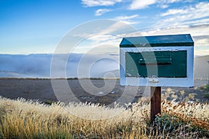 Wooden vintage mailbox in beautiful nature landscape, golden dried grass with small flower and sea of fog and blue sky in the