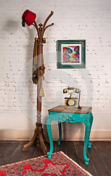Wooden vintage side table, golden antique telephone, and coat hanger stand with red fez and scarf