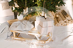 Wooden vintage sleigh with a blanket and gifts under the Christmas tree. Christmas decor in the interior of the house