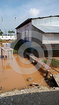 A wooden walk way from a tin sheded room over stagnant rain water in a construction site.