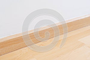 Wooden wall base skirting, finishing material with wood laminate floor and white mortar wall. Empty room with white wall and