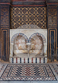 Wooden wall decorated with painted floral patterns, double embedded arched niche and marble floor decorated with geometric pattern photo