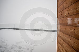 Wooden wall on terrace covered by snow at cable car station Birg on Schilltorn mountain with foggy background