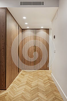 Wooden wardrobe with smooth doors in a room with herringbone oak flooring, spotlights in the false ceiling and ducted air photo