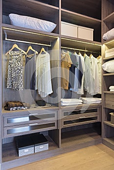 wooden wardrobe in walk in closet with clothes