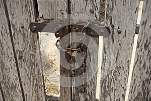 Wooden weathered gate locked with rusty chain and lock.