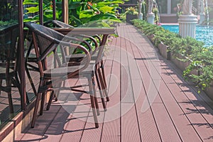 Wooden weave brown chairs and table place on terrace beside swimming pool.