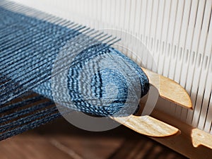 Wooden weaving shuttle with blue yarn is inserted in open shed. Separation between upper and lower warp yarns through which the