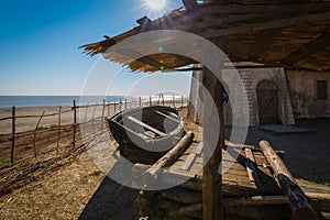 The wooden well, old holey boat and dilapidated hut on the seashore on a sunny day