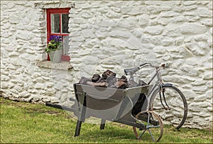 Wooden wheel barrow of peat outside a traditional irish cottage