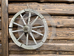 Wooden wheel from an old horse-drawn carriage. The wheel hangs on a wooden fence, as a decoration of the yard. Household items in