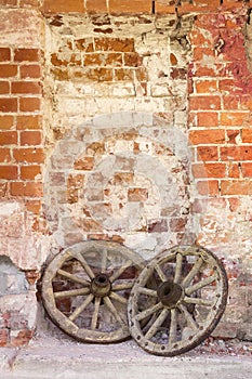 Wooden wheels from an old cart lie against the background of an old brick wall.
