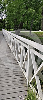 Wooden white footbridge over the river in summer park.