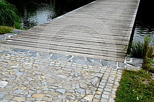 wooden wide pedestrian bridge over the river pond lake, without railings design of gray oak wood connects to the stone path of