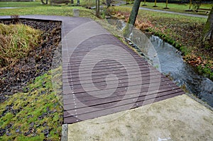 Wooden wide pedestrian bridge over the river pond lake, without railings design of gray oak wood connects to the stone path of nat