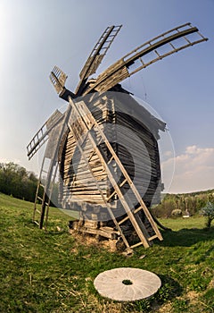 Wooden windmill and millstone on the hillside against the backdrop of the rural landscape.