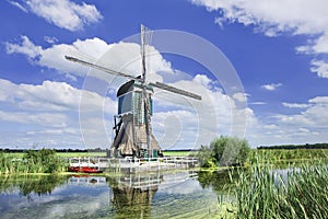 Wooden windmill near a canal on a summer day with blue sky and clouds, Netherlands.