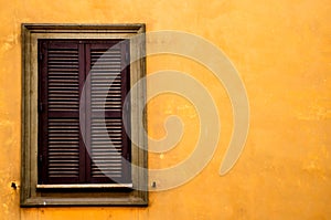 A wooden window on the bright orange wall of one of the houses of Rome. Italy