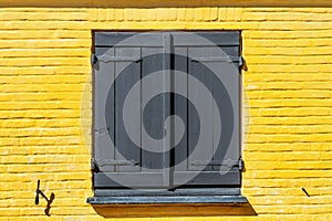 Wooden window with shutters on a yellow, brick facade.