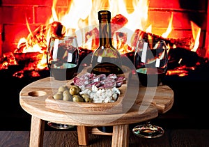 Wooden wine table with appetizers for wine against electric fireplace. Wine glasses with blue cheese, fuet sausage