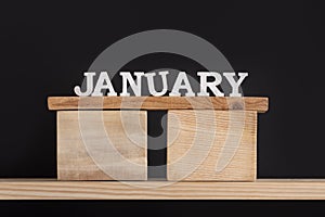 Wooden winter calendar months - January. Wooden letters and stand on black background