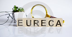 Wooden word block EURECA on white background with glasses and magnifier