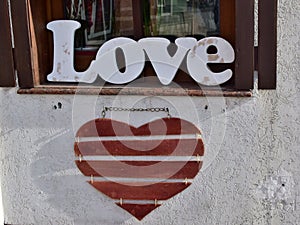 Wooden word `Love` standing on the windowsill and red wooden heart hanging on the wall in the city street photo