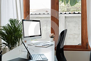 Wooden work desk with pc computer with blank screen, books, modern interior of cozy cabinet, table for businessman or