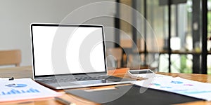 A wooden working desk is surrounding by a white screen computer laptop.