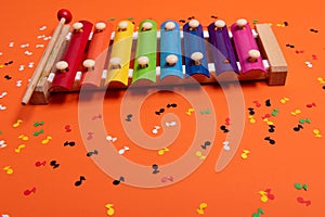 Wooden xylophone in rainbow colors for children an  on orange. Paper colorful musical notes surrounding