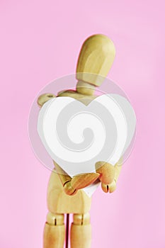 Wooden yellow mannequin holding a white heart in his hands